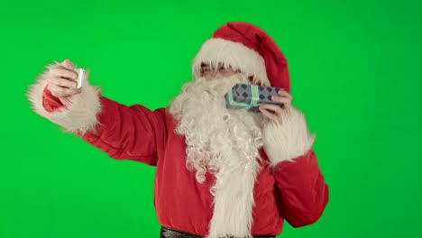 Weihnachtsmann-mit-einem-großen-Geschenk,-das-ein-Selfie-auf-dem-Smartphone-auf-einem-Green-Screen-Chrome-Key-macht