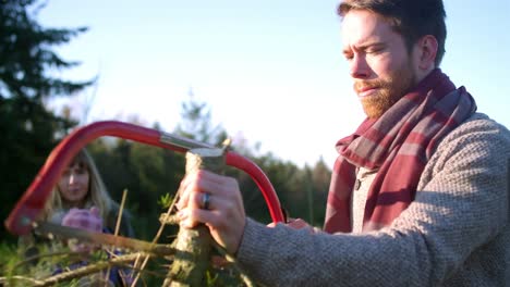 Young-man-sawing-branches-off-a-Christmas-tree-while-his-wife-and-baby-watch