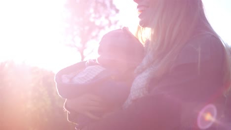 Un-joven-papá-habla-con-su-bebé-mientras-mamá-la-sostiene,-en-una-granja-de-árboles-de-Navidad,-destello-de-lente