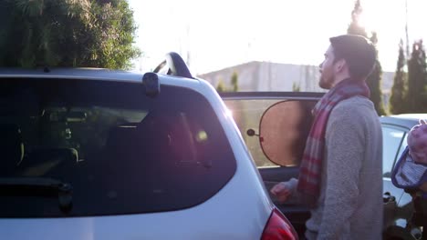 A-young-family-putting-a-Christmas-tree-on-top-of-their-car-at-a-farm,-lens-flare