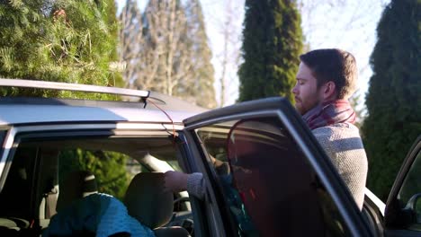 Junger-Mann-binden-einen-Weihnachtsbaum-zum-Auto-mit-Seil