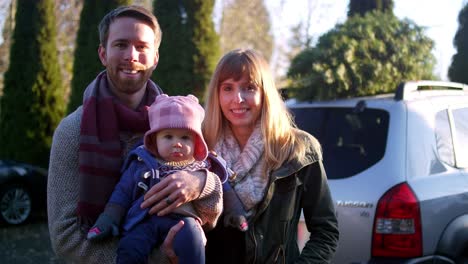 Portrait-of-a-young-mother,-father-and-baby-in-front-of-their-car-with-Christmas-tree-on-top
