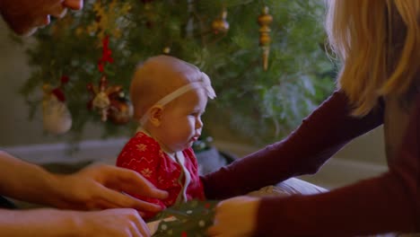 Eltern-öffnen-geschenke-mit-ihrem-Baby-vor-dem-Baum-am-Weihnachtsmorgen