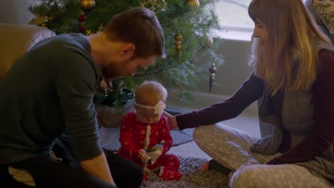 Parents-opening-presents-with-their-baby-in-front-of-the-tree-on-Christmas-morning