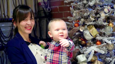 Mutter-mit-ihrem-Baby-in-den-Armen,-die-neben-einem-Weihnachtsbaum-steht.-Neujahr