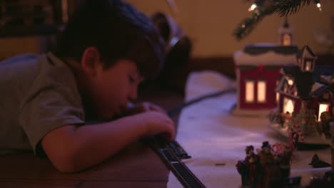 Little-boy-putting-together-train-tracks-in-front-of-the-christmas-tree