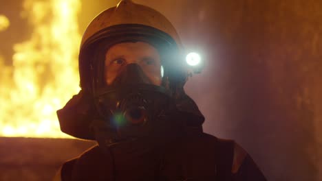 Portrait-Shot-of-a-tapve-Fireman,-der-in-einem-brennenden-Gebäude-steht,-das-sich-hinter-ihm-verbirgt.-Offene-Flammen-und-Rauch-im-Hintergrund.