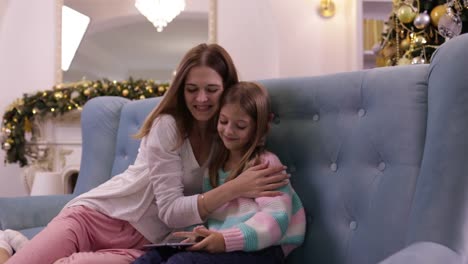 Mutter-mit-Tochter-auf-Couch-mit-Tablet-Computer-Happy-Smiling-junge-Familie-in-der-Nähe-dekorierten-neuen-Jahr-Weihnachtsbaum