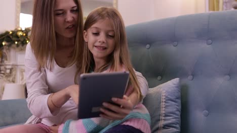 Mutter-mit-Tochter-auf-Couch-mit-Tablet-Computer-Happy-Smiling-junge-Familie-in-der-Nähe-dekorierten-neuen-Jahr-Weihnachtsbaum