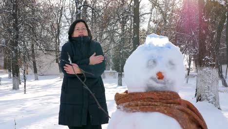 Joven-mujer-edificio-muñeco-de-nieve-en-el-parque.-En-el-invierno