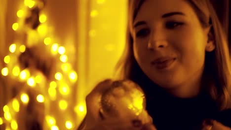 Portrait-of-a-young-woman-with-fairy-lights-in-the-house-shaking-the-snow-globe