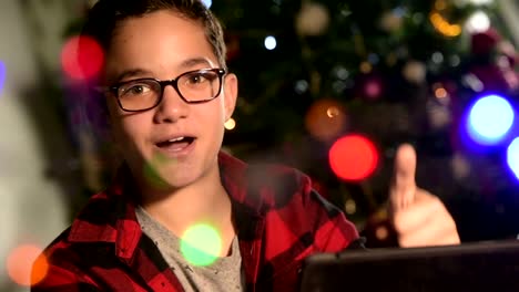Young-Boy,-child-looks-to-the-tablet-lying-on-sofa.On-the-background-lights-garlands
