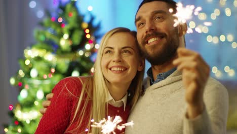 Glückliches-Paar-leichte-Wunderkerzen-und-Lächeln.-Im-Hintergrund-Weihnachtsbaum-und-Zimmer-mit-Lichtern-geschmückt.