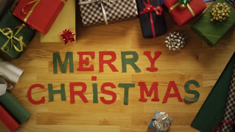 Top-View-Time-Lapse-of-a-Man-Cutting-Letters-for-Words-"Merry-Christmas"-and-laying-Them-on-The-Wooden-Table-With-Gift-Wrapped-Boxes.-Dynamic-Camera.