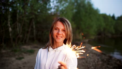 Portrait-of-young-smiling-woman-with-sparkler-celebrating-at-beach-party