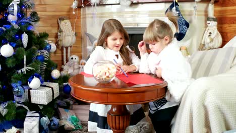 Carta-para-Papá-Noel,-dos-chicas,-hermanas-escribir-y-dibujar,-chicas-sentarse-cerca-de-la-chimenea,-los-niños-en-la-casa-cerca-de-árbol-de-Navidad