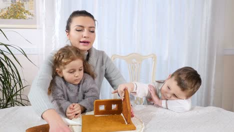 Joven-madre-con-los-niños-hace-una-casa-de-pan-de-jengibre-en-la-cocina