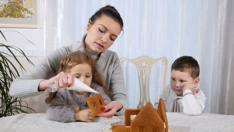 Young-mother-with-two-children-makes-a-gingerbread-house
