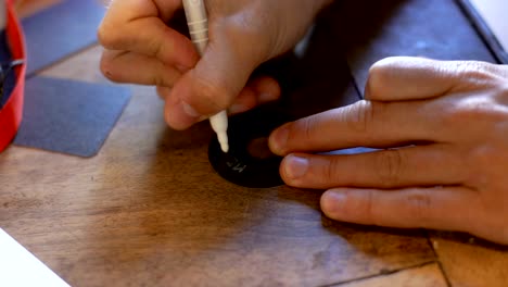 Young-adult-man-writing-christmas-card-on-black-label-with-white-marker-on-old-wooden-table-in-cozy-home-indoor