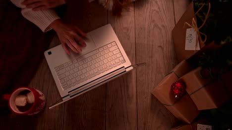 Junge-rothaarige-Frau-einkaufen-online-über-mit-Laptop-unter-Weihnachtsbaum