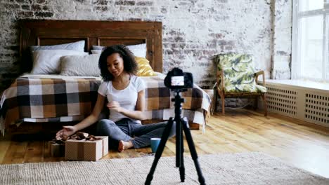 Young-cheerful-mixed-race-girl-recording-video-blog-about-packing-christmas-gift-box-at-home