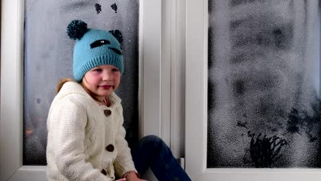 Small-girl-sits-on-windowsill-behind-the-frozen-window.