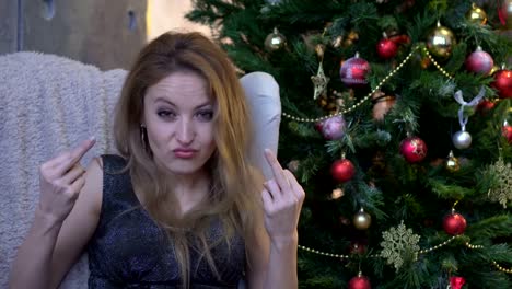 Stilvolle-junge-Frau-mit-rosa-Lippenstift-sitzen-in-der-Nähe-von-Weihnachtsbaum-und-zeigt-Mittelfinger