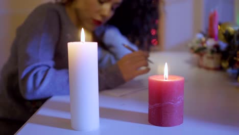 Burning-candles-at-table,-woman-writes-a-wish-list-at-blurred-background