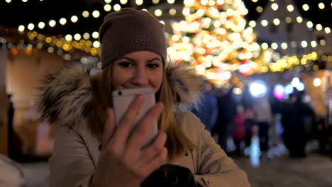 Joven-sonriente-mujer-Selfie,-permanente-en-el-mercado-de-Navidad-con-iluminaciones