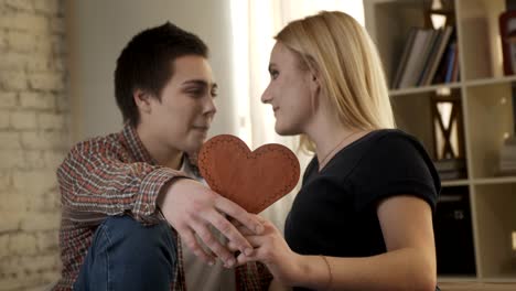 Two-young-lesbians-cute-look-at-each-other,-holding-a-heart-sign-in-their-hand,-smiling,-laughing-60-fps