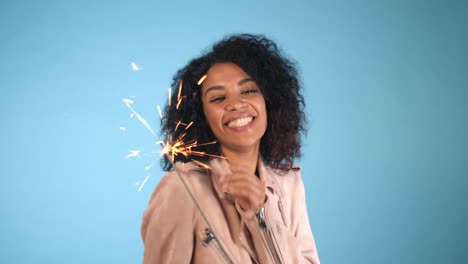 Brillante-fuego-de-Bengala-en-la-mano-de-la-mujer-afroamericana-sobre-fondo-azul.-Concepto-de-vacaciones-de-Navidad.-Joven-bonita-a-chica-con-peinado-afro-celebrando,-sonriendo,-disfrutando.-4k