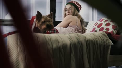 Beautiful-woman-lays-on-bed-and-straightens-the-Santa's-cap-on-her-dog