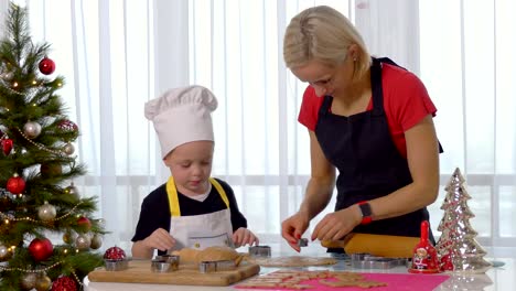 Der-kleine-junge-Kind-hilft-Mutter-zu-Weihnachten-Ingwer-Keks-in-leichte-Küche-kochen.-Glückliche-Familie-Mutter-30-35-Jahren-und-Kind-3-4-ausrollen-Teig-und-schneiden-Sie-Cookies-im-Hause.-Beziehung-und-Liebe-Konzept