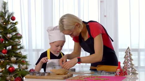 The-little-kid-boy-helps-mother-to-cook-Christmas-ginger-biscuit-in-light-kitchen.-Happy-family-mom-30-35-years-and-child-3-4-roll-out-dough-and-cut-out-cookies-at-home.-Relationship-and-love-concept