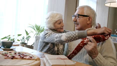 Elderly-Woman-Putting-Scarf-on-Man-at-Christmas-Dinner-in-Cafe