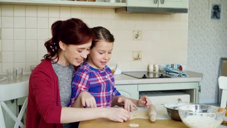 Smiling-mother-and-cute-daughter-making-cookies-together-using-bakery-forms-while-sitting-in-modern-kitchen-at-home.-Family,-food-and-people-concept
