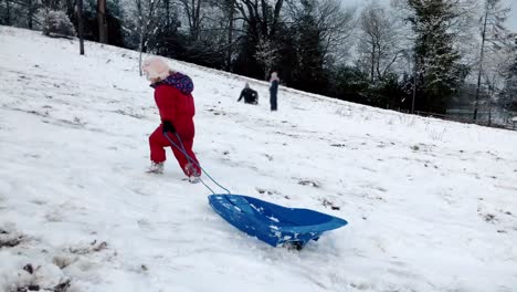 Junge-kleinkind-mädchen-Ziehen-eines-Schlittens-auf-einem-schneebedeckten-Hügel