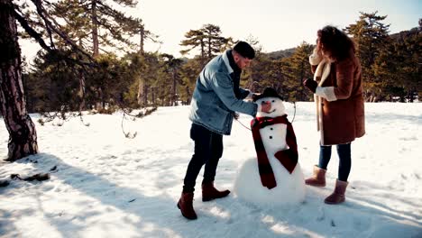 Junges-Paar-macht-Schneemann-im-tief-verschneiten-Bergwald