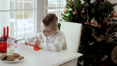 Fröhlicher-junge-schreibt-einen-Brief-an-den-Weihnachtsmann-und-isst-cookies