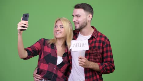 Young-couple-taking-selfie-while-holding-paper-sign-together
