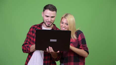 Young-happy-couple-smiling-while-using-laptop-together