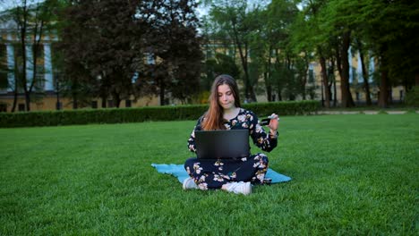 Ein-Weibchen-im-Sommerkleid-mit-einem-Laptop-und-einem-Kreditkarten-im-freien