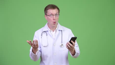 Médico-de-hombre-sorprendido-usando-teléfono-móvil-mirando-feliz