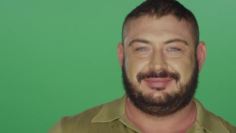 Muscular-man-attempts-to-make-silly-faces,-on-a-green-screen-studio-background