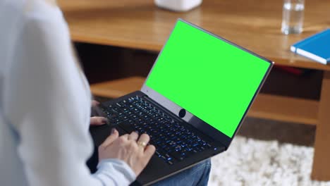 Über-die-Schulter-Schuss-eine-Frau-an-einem-Notebook-arbeitet-mit-Greenscreen-Mock-up-drauf.-Sie-hält-den-Laptop-auf-dem-Schoß.