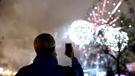 Closeup-de-silueta-de-hombre-viendo-y-fotografiando-fuegos-artificiales-explotan-sobre-smartphone-cámara-al-aire-libre