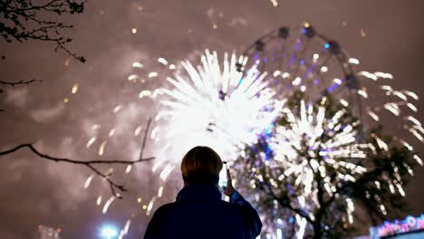 Closeup-de-silueta-de-hombre-viendo-y-fotografiando-fuegos-artificiales-explotan-sobre-smartphone-cámara-al-aire-libre