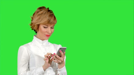 Young-attractive-woman-works-on-smartphone-and-smiles-on-a-Green-Screen,-Chroma-Key