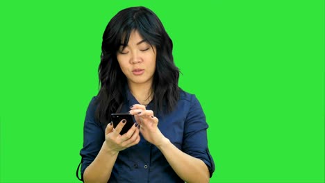 Nachdenklich-asiatische-Geschäftsfrau-lesen-Präsentation-auf-Smartphone,-Blick-in-die-Kamera-auf-einem-Green-Screen,-Chroma-Key