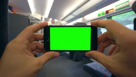 Manos-sosteniendo-un-teléfono-con-una-pantalla-verde-en-el-tren